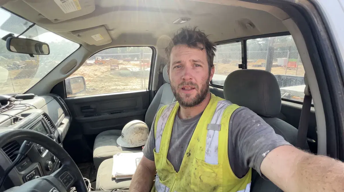 Travis, a site laborer applicant in a hi-vis vest, answering an interview question from his truck on a lunch break